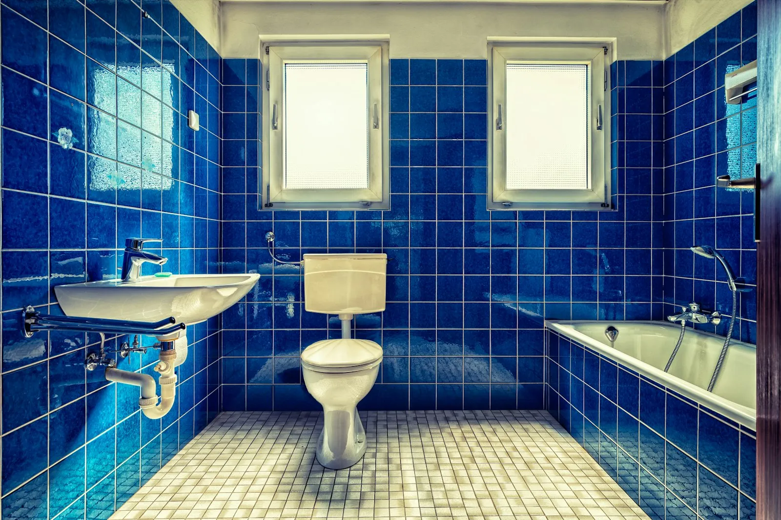 Kamar mandi lama bergaya 90an dengan keramik biru tua dan sanitari usang